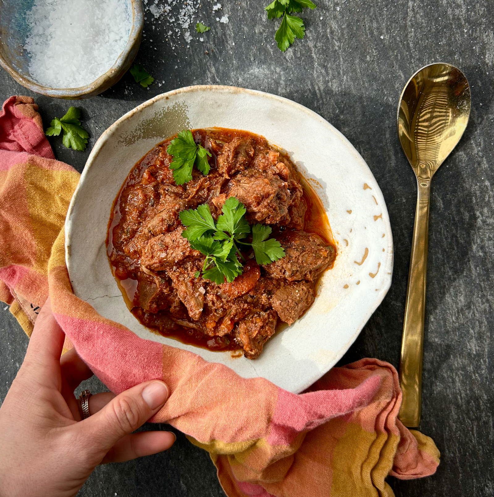 Hearty chunks of beef in a thick tomato stew with carrots and fresh herbs, served in a rustic bowl