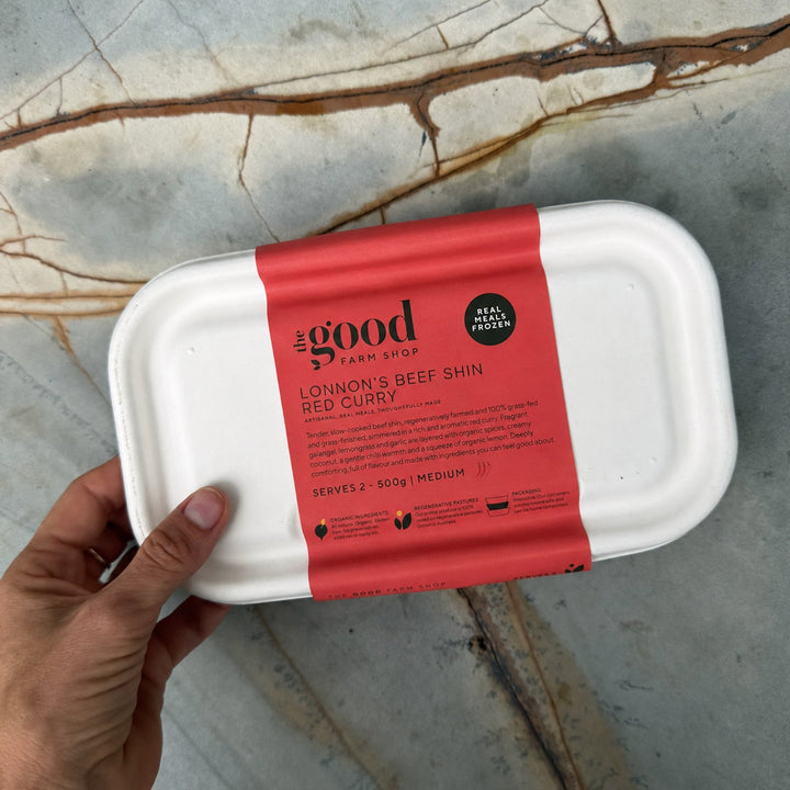 A hand holding a white paperboard food container with a red label that reads &