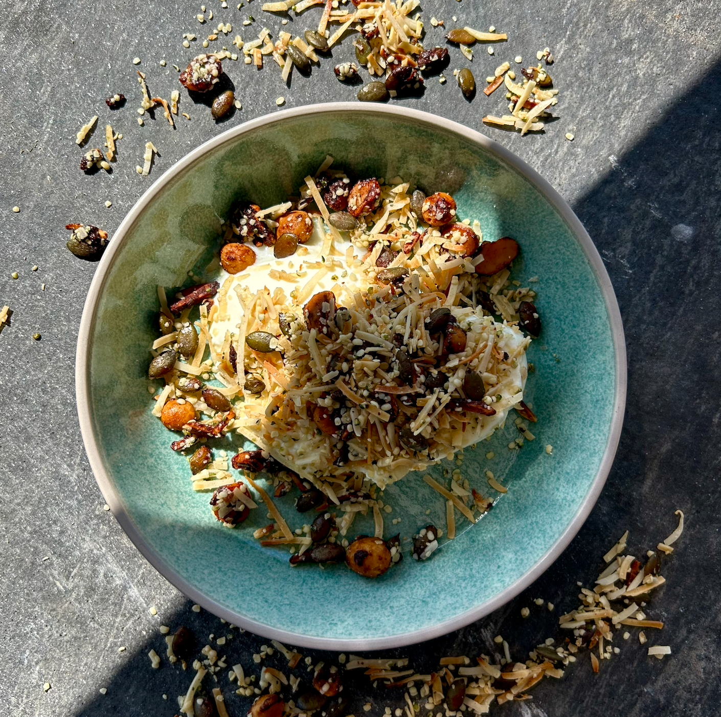 A bowl of granola topped with nuts, seeds, and honey, served with yoghurt.