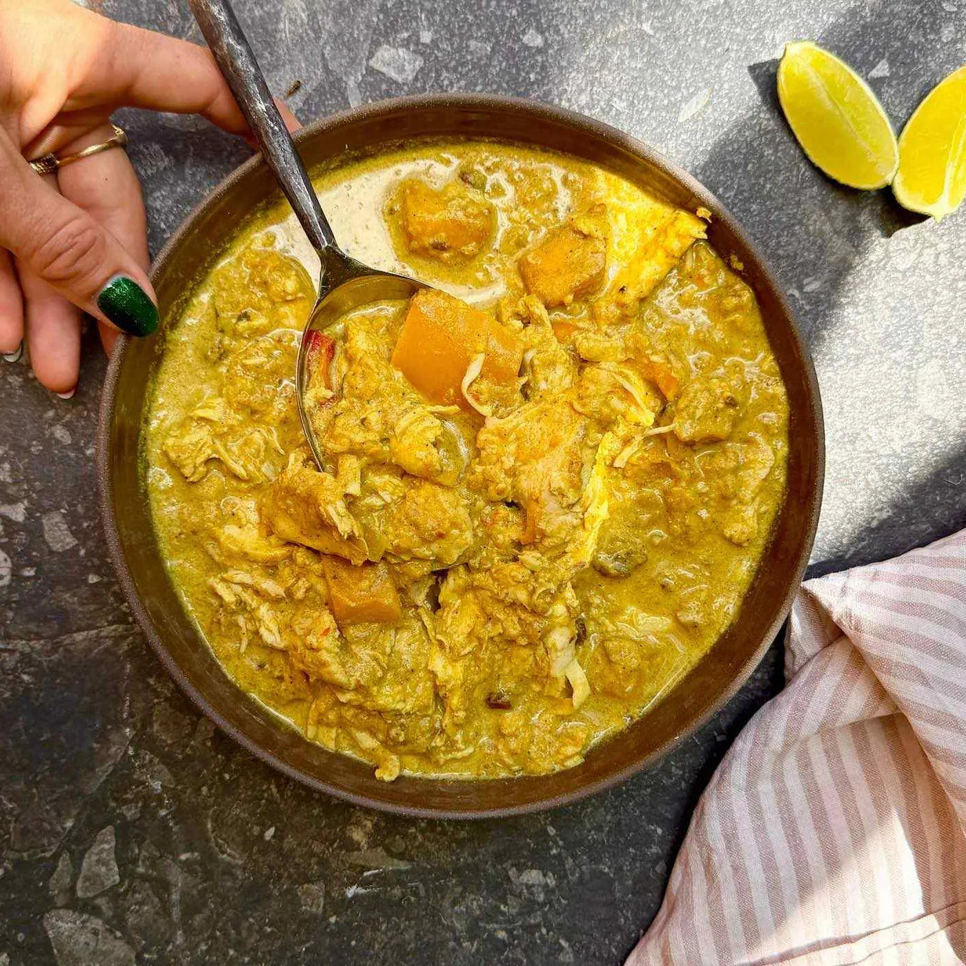Mango chicken curry in brown bowl with lemon wedges in the background