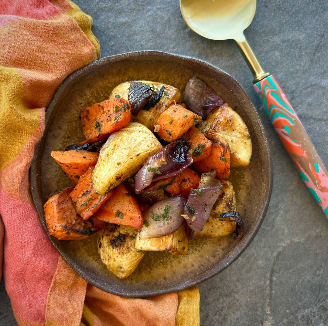 A plate of roasted vegetables including carrots, sweet potato, potato, and red onion, garnished with herbs and spices.