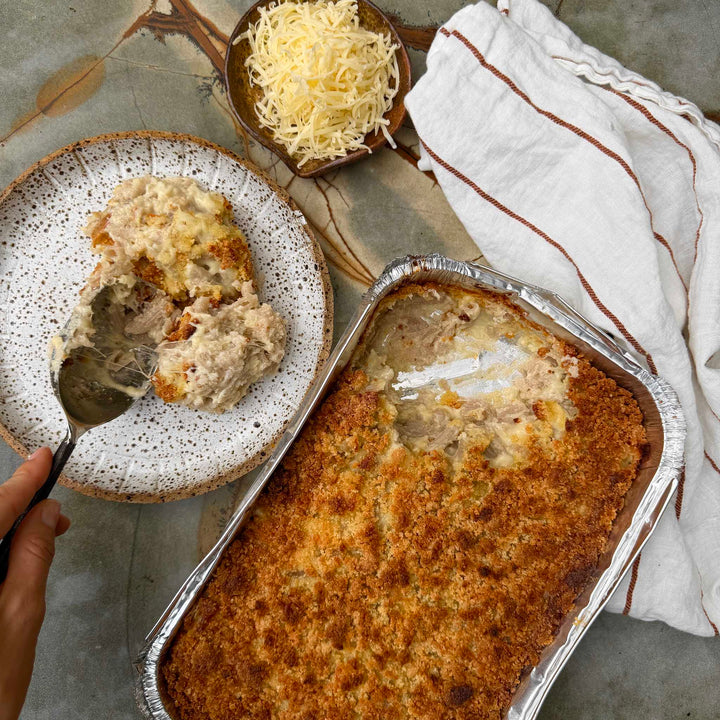 Baked dish in a foil pan with a portion on a plate, accompanied by grated cheese and a striped towel.