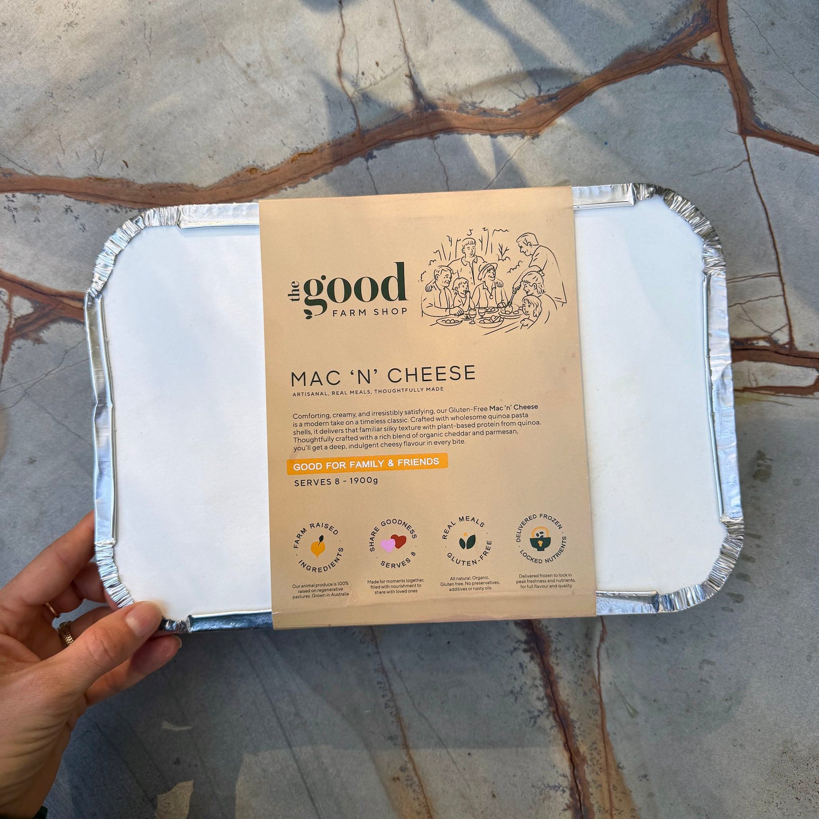 Mac 'n' Cheese packaging from the Good Farm Shop held by a hand on a stone surface.
