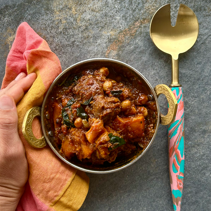 A bowl of Moroccan Lamb stew with chunks of lamb, pumpkin, and spices, served with a spoon and a colorful napkin on the side.