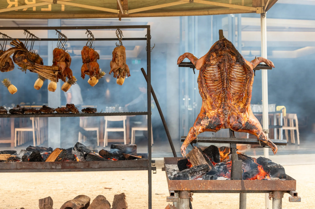 Roasted animal on a spit over an open flame with a metal stand in a kitchen setting.