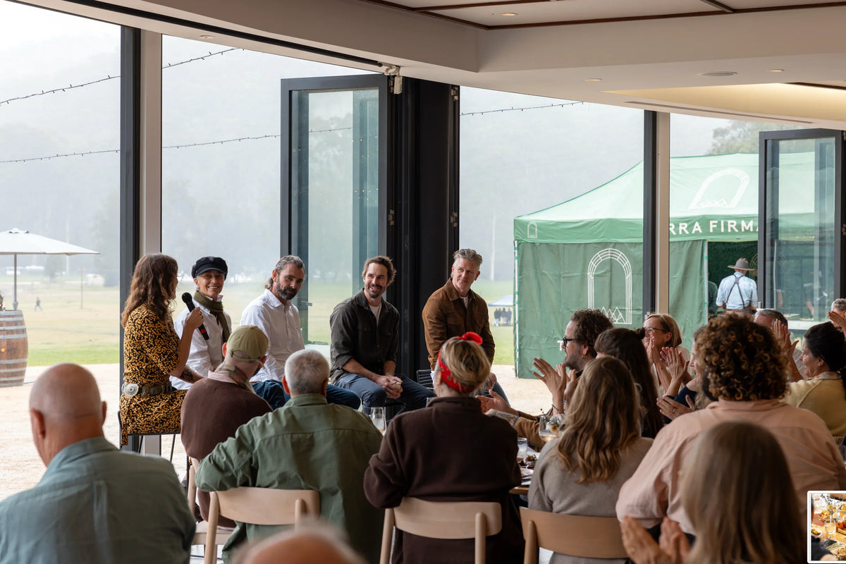 Group of people gathered in a modern building with large windows, listening to a speaker.