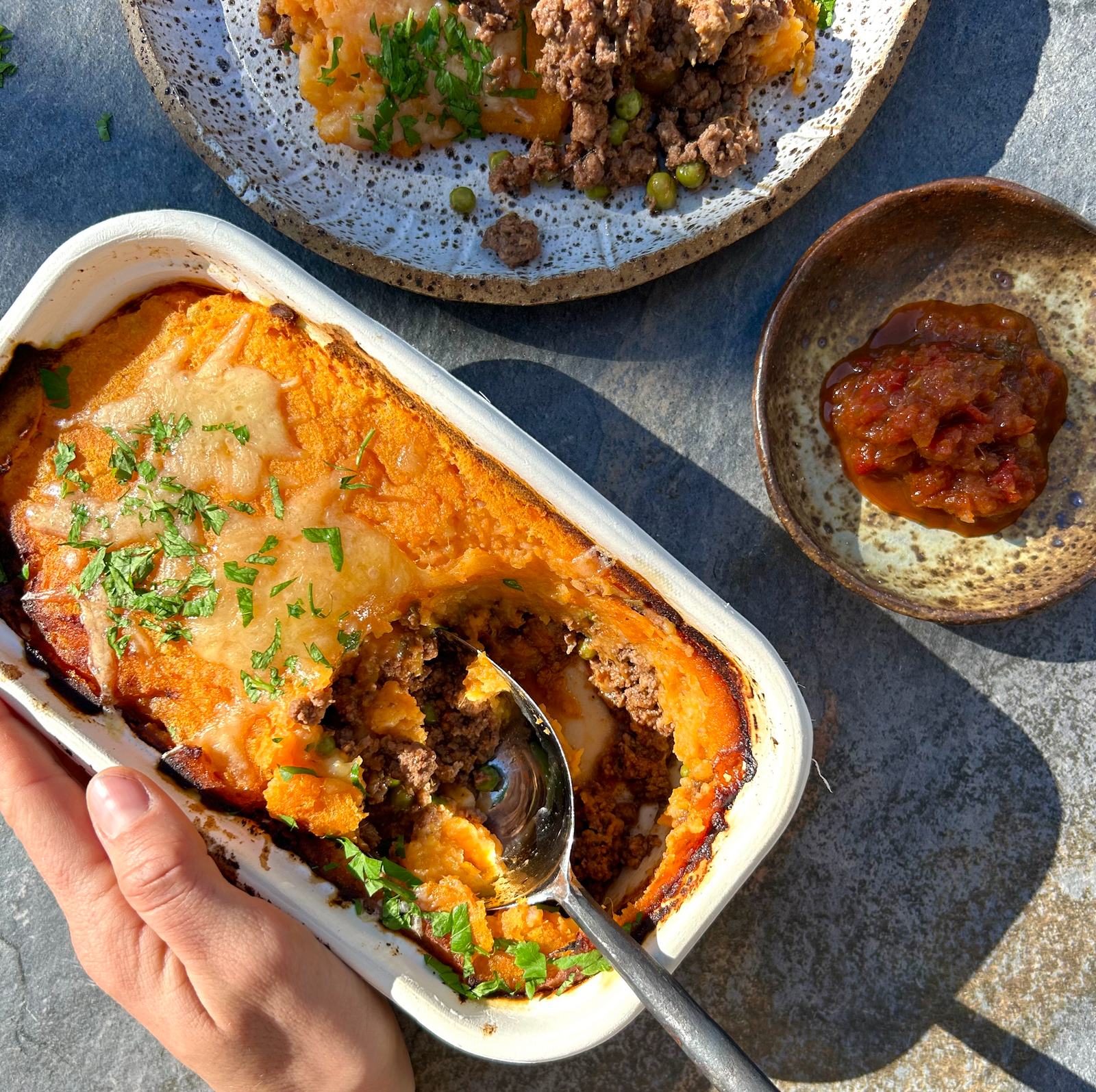 A serving of Shepherd's Pie in a white compostable container, with a spoonful taken out, showcasing the layers of lamb, vegetables, and mashed potatoes.