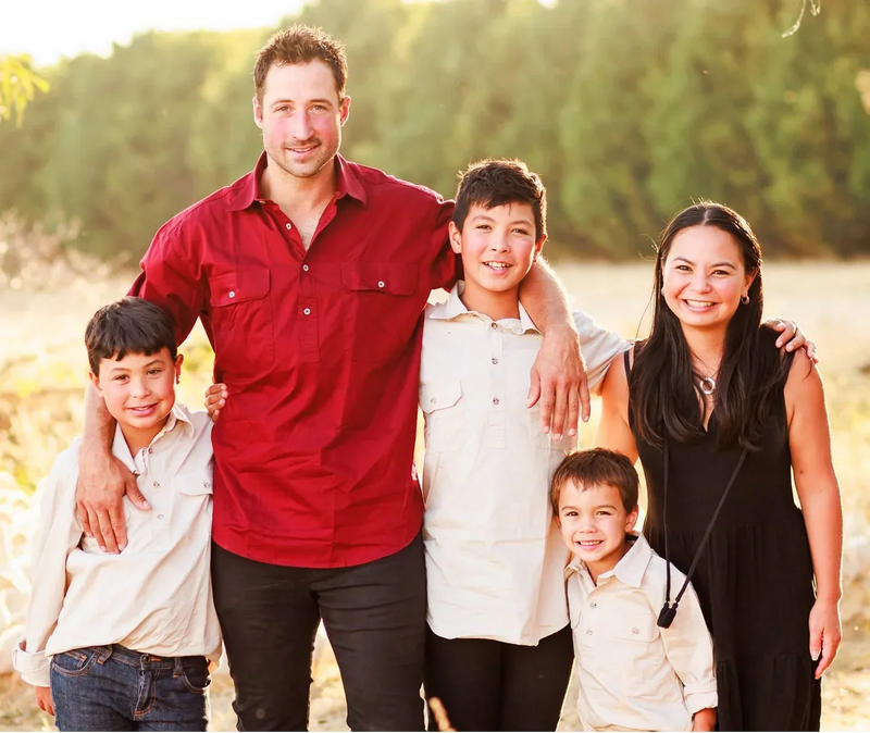 Family of five posing together in a natural setting with trees and grass.