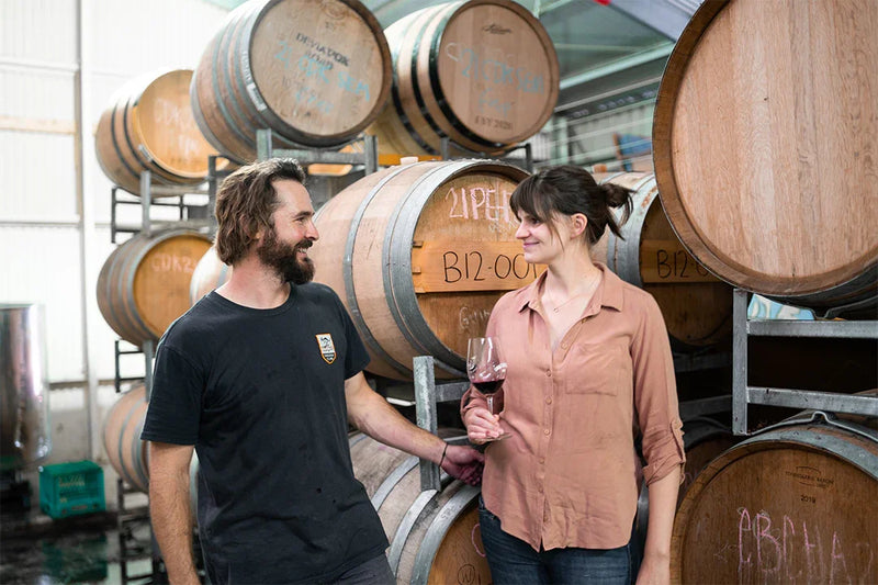Two people standing among wooden barrels in a warehouse setting