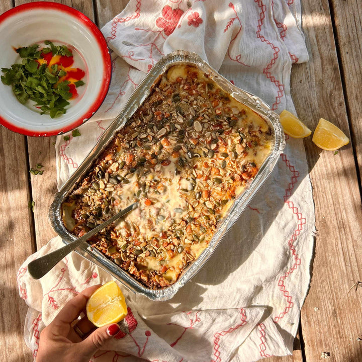 Baked dish in a foil pan on a wooden surface with a hand holding a lemon.