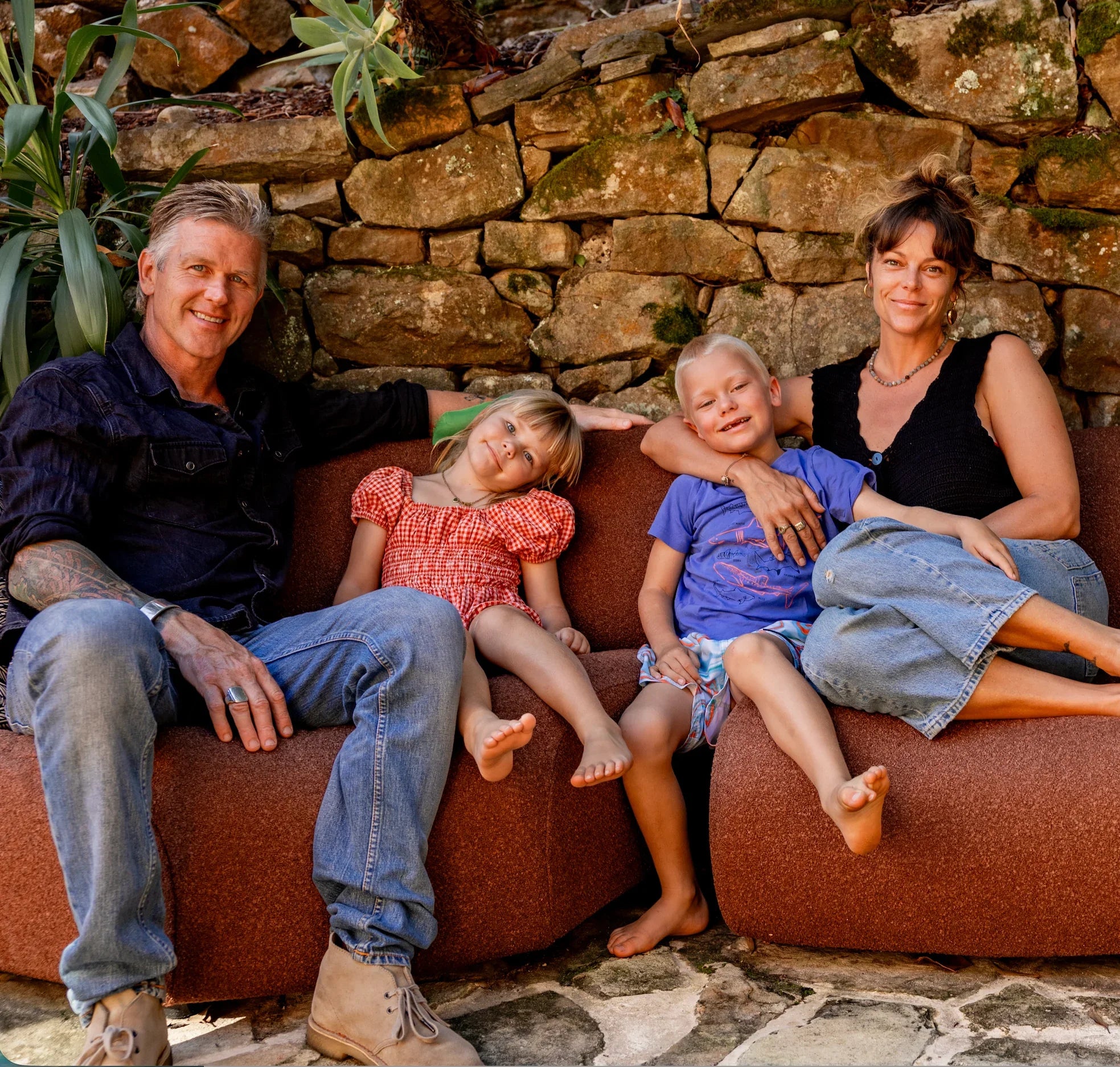 Family of four sitting on a brown couch against a stone wall.
