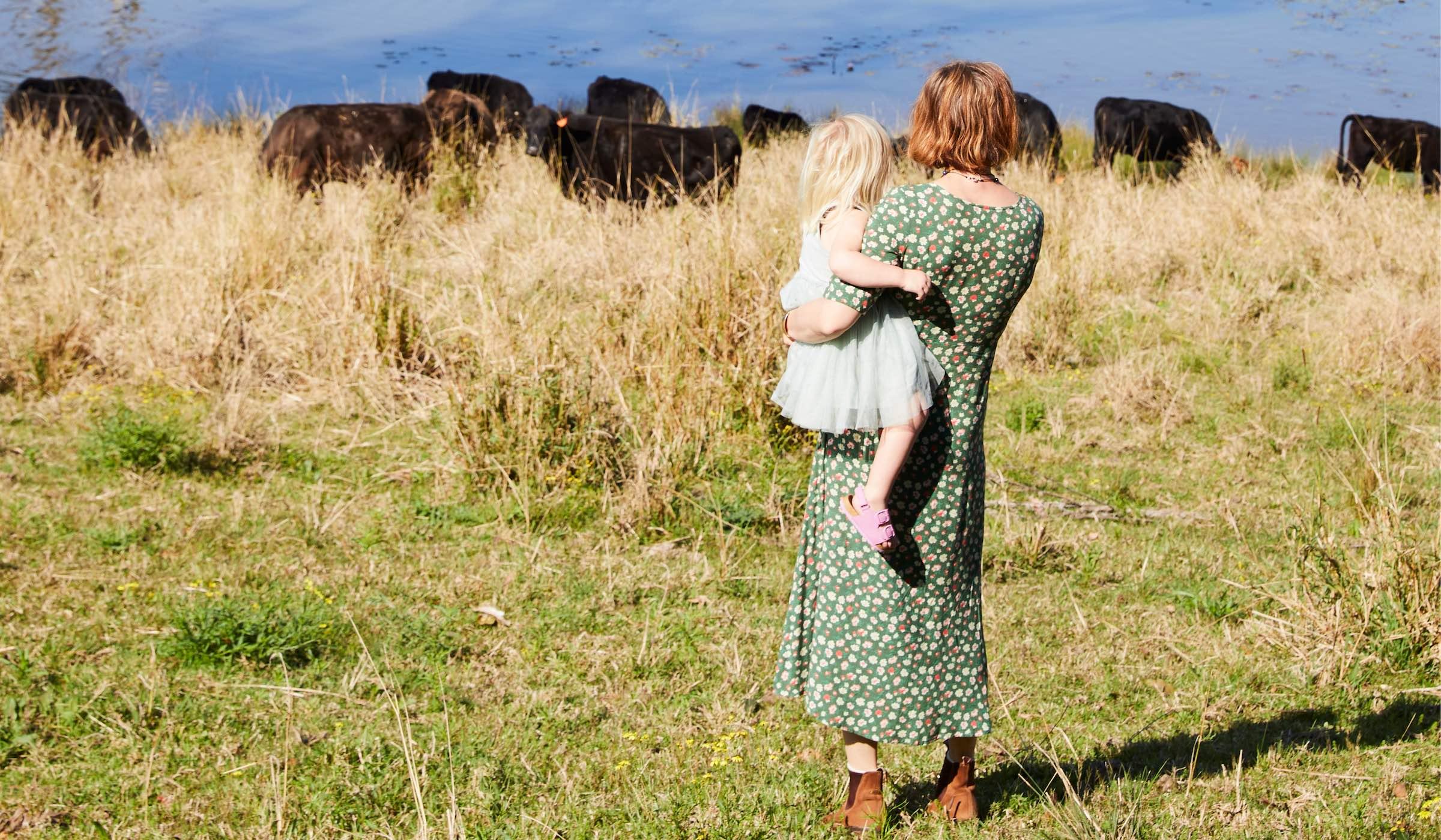 Woman holding a child in a field with cows in the background