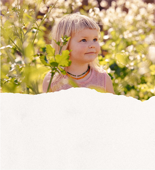Young girl with blonde hair standing in a field of green plants.